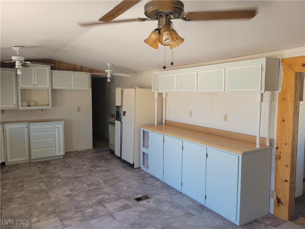 7950 South Wildhorse Road Pahrump, NV 89061 - Photo 9 of 28 Kitchen with light countertops, lofted ceiling, white fridge with ice dispenser, white cabinets, and stone finish floors