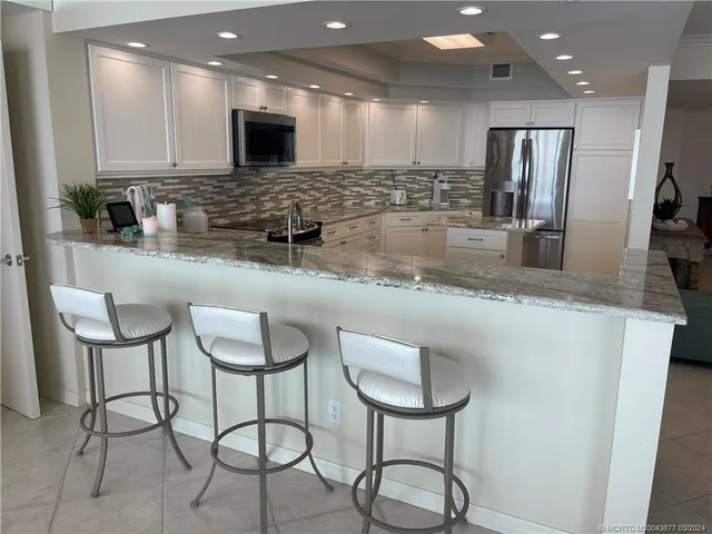 a large kitchen with granite countertop a counter space chairs stainless steel appliances and cabinets