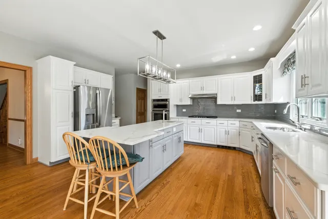 a large kitchen with stainless steel appliances granite countertop a sink dishwasher a stove a dining table and chairs with wooden floor