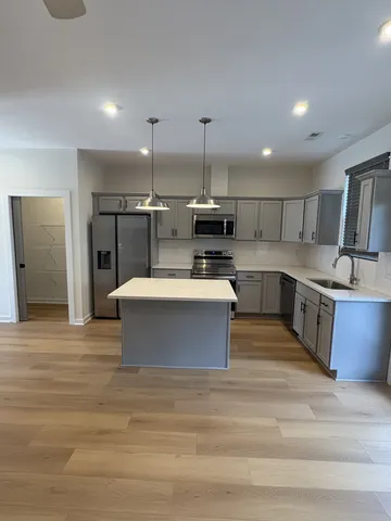 a large kitchen with stainless steel appliances kitchen island a stove a sink dishwasher a refrigerator and white cabinets with wooden floor