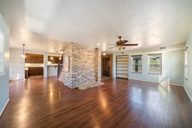 an empty room with wooden floor ceiling fan and windows