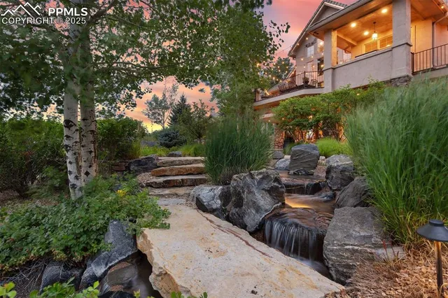 a view of a patio with table and chairs under an umbrella with large trees
