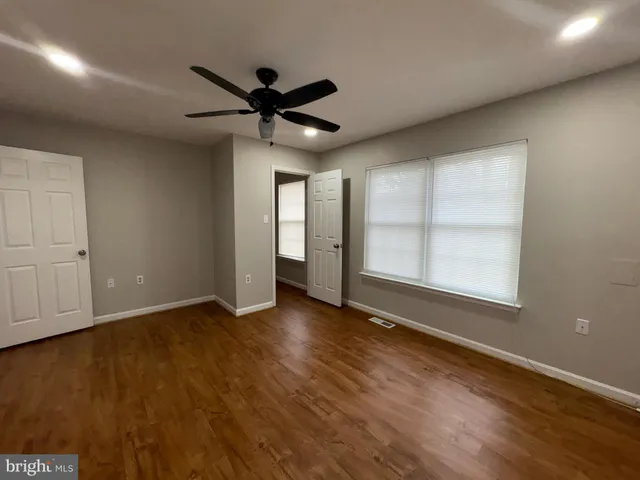 an empty room with wooden floor fan and windows