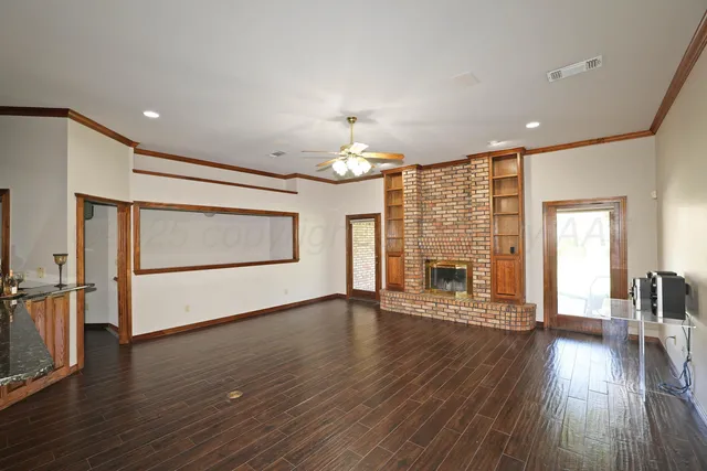 an empty room with wooden floor fireplace and windows