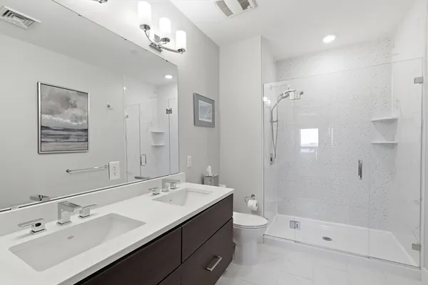 a bathroom with a double vanity sink a toilet a shower and a mirror