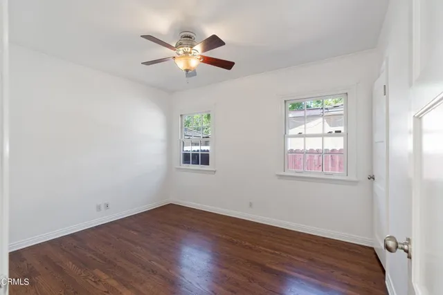 an empty room with wooden floor fan and windows