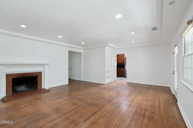 an empty room with wooden floor fireplace and windows