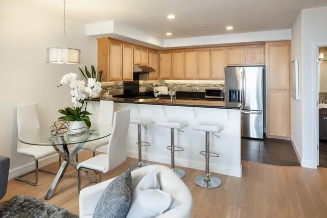 a kitchen with stainless steel appliances granite countertop a refrigerator a stove a sink counter tops and chairs with wooden floor