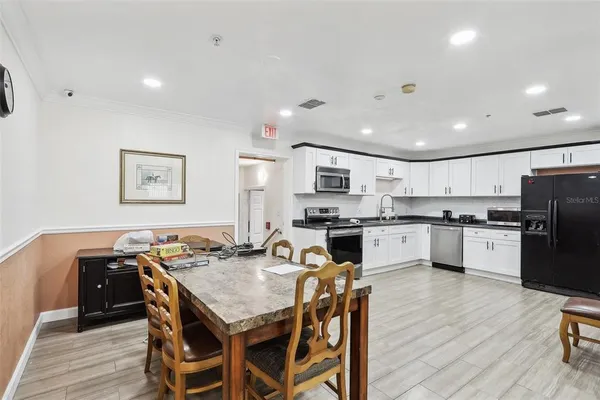 a kitchen with stainless steel appliances kitchen island granite countertop a refrigerator a stove top oven a sink dishwasher and white cabinets with wooden floor