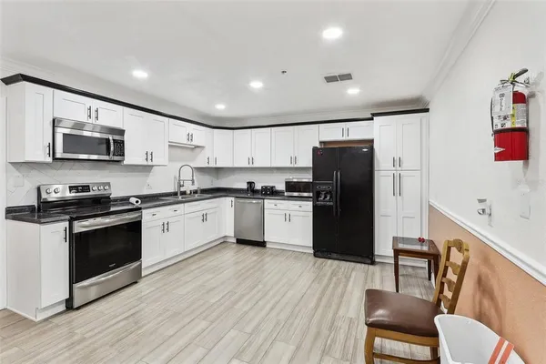 a large kitchen with a refrigerator a stove top oven a sink dishwasher and white cabinets with wooden floor