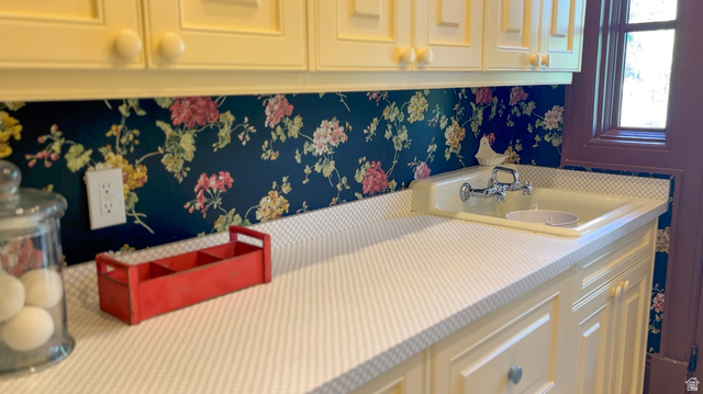 426 West Center Street Parowan, UT 84761 - Photo 75 of 107 Cream cabinetry with round knobs, floral wallpaper backsplash, light-toned countertop, and an integrated sink with a chrome faucet