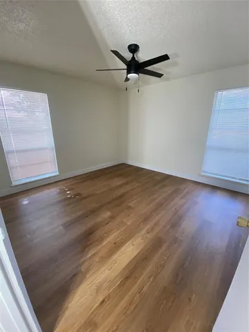 an empty room with wooden floor fan and windows