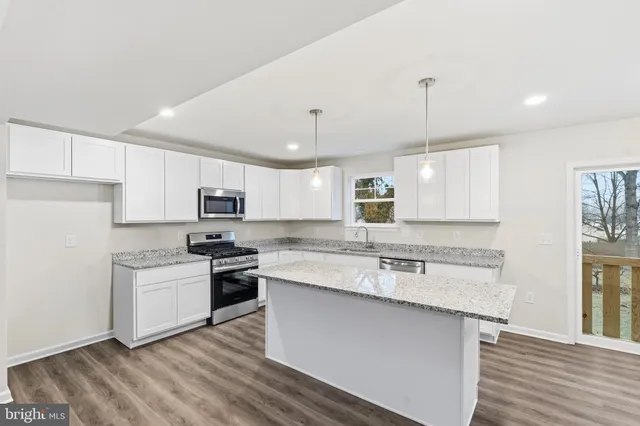 a kitchen with stainless steel appliances granite countertop a sink a stove a refrigerator and island with wooden floor