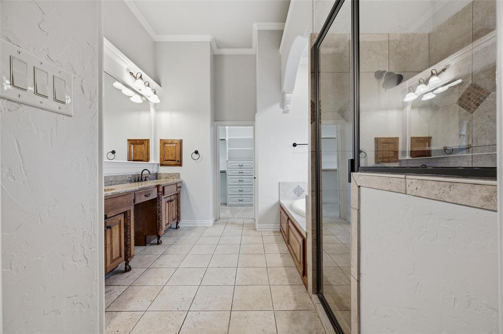 620 Highview Lane Hurst, TX 76054 - Photo 26 of 40 Spacious bathroom featuring dual wood-finish vanities with granite countertops, a walk-in shower with glass enclosure, an integrated soaking tub, and tile flooring