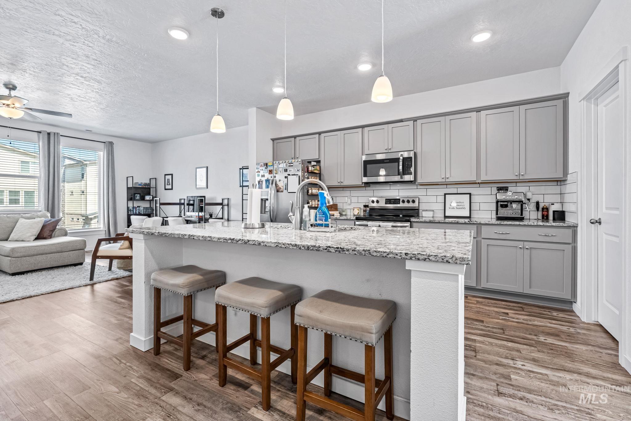 3084 North Network Lane Boise, ID 83704 - Photo 1 of 1 Kitchen with gray cabinets, a breakfast bar area, light stone countertops, stainless steel appliances, and a textured ceiling