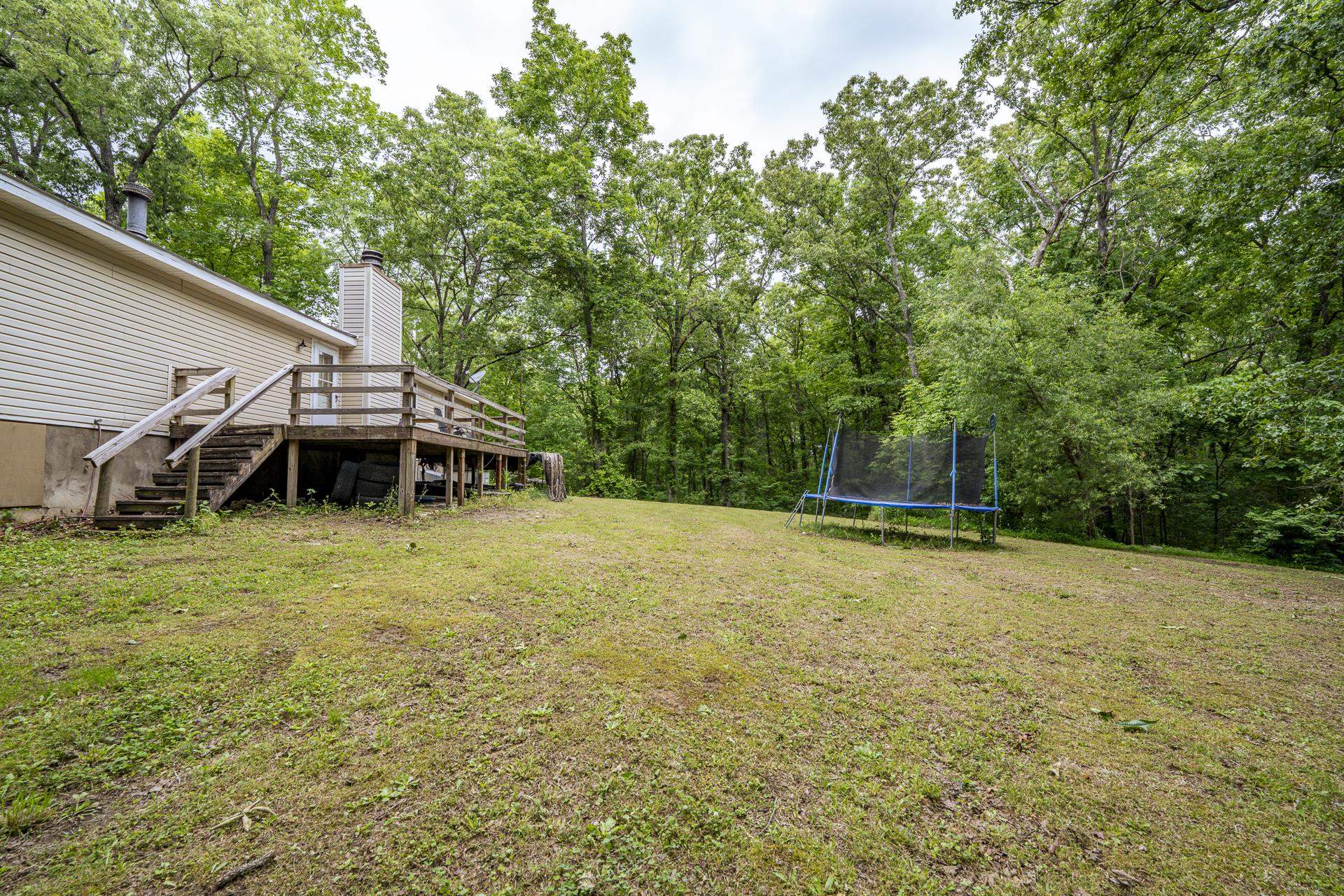 259 Oakview Drive Adamsville, TN 38310 - Photo 28 of 32 Expansive backyard featuring a large wooden deck with railings and stairs, a beige sided exterior, a prominent chimney structure, and a backdrop of mature trees