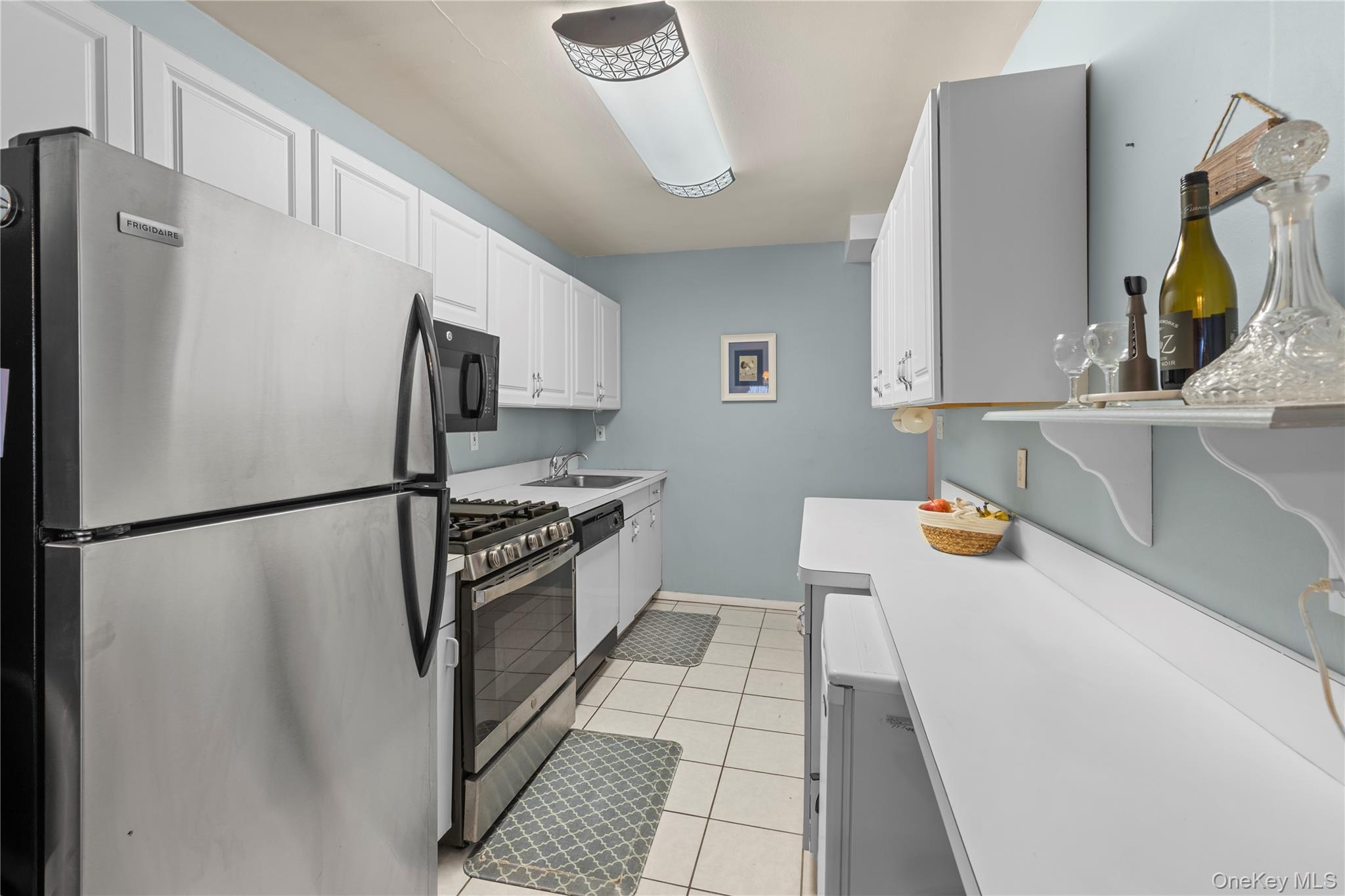 711 Shore Road, Unit 3B Long Beach, NY 11561 - Photo 7 of 20 Kitchen with appliances with stainless steel finishes, white cabinets, light tile patterned floors, and light countertops