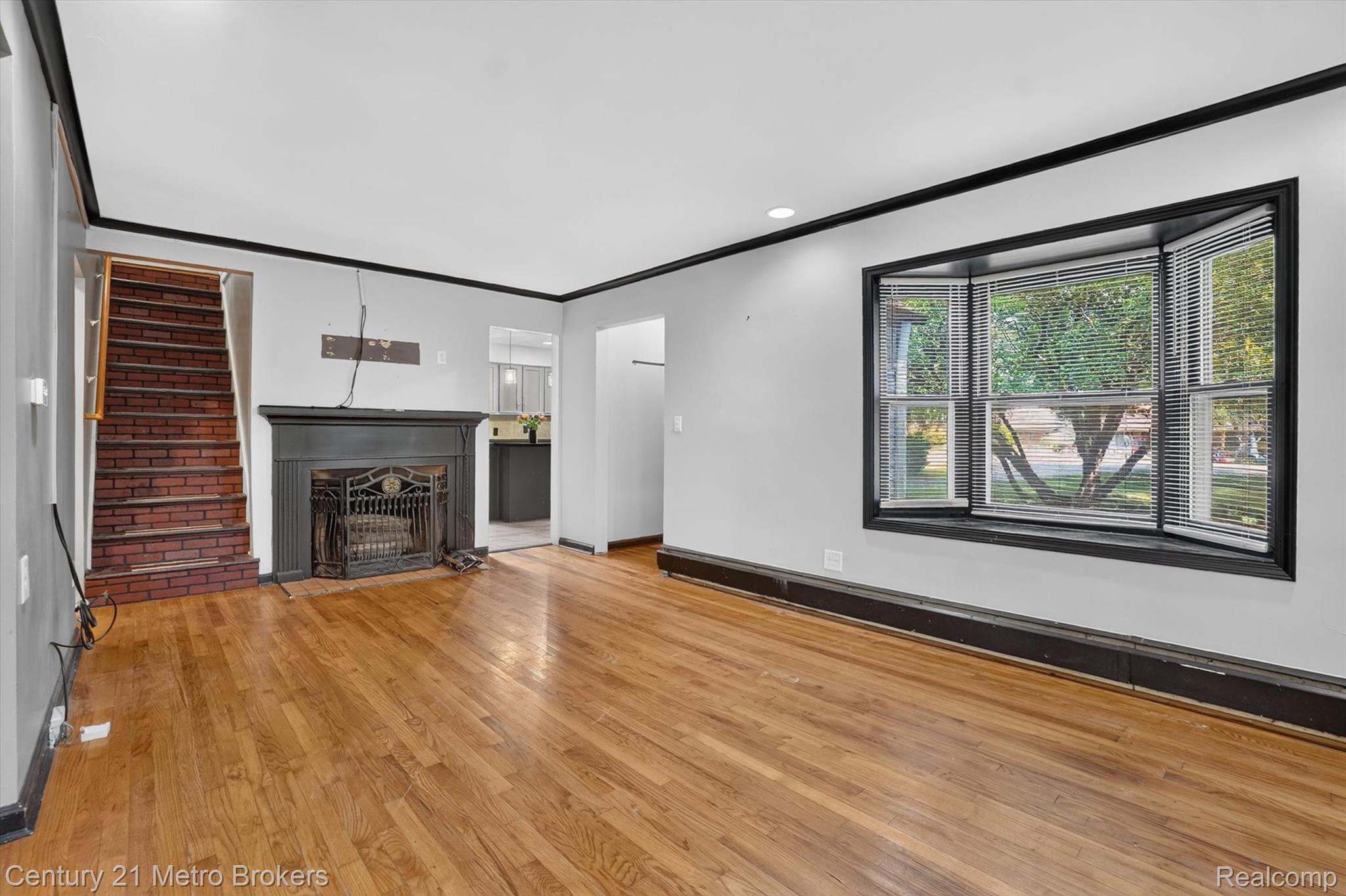 4575 Brockway Road Saginaw, MI 48638 - Photo 11 of 44 Hardwood flooring, bay window, fireplace with dark mantel, brick-faced staircase, and crown molding