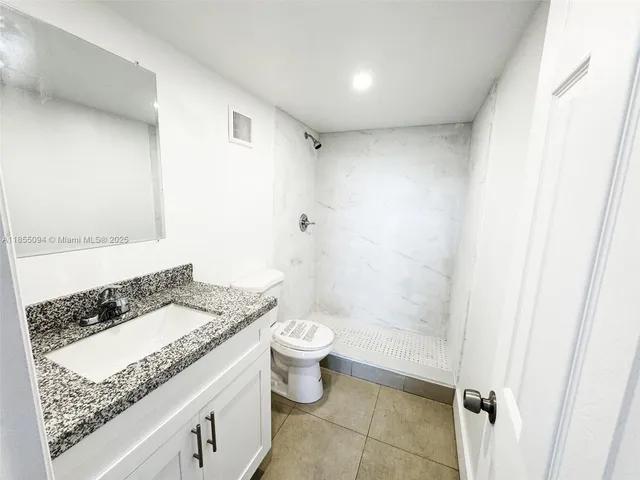 a bathroom with a granite countertop sink a toilet a mirror and shower