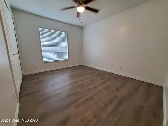 an empty room with wooden floor fan and windows