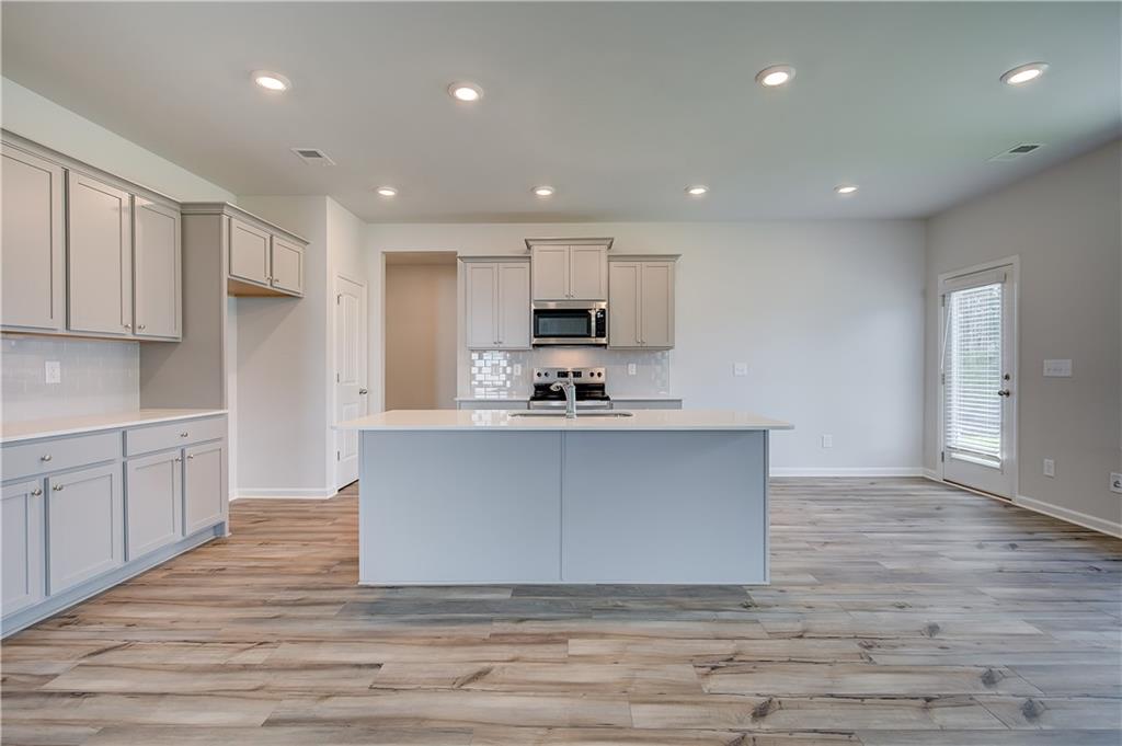 149 St Anne's Place Covington, GA 30016 - Photo 12 of 30 a large kitchen with stainless steel appliances granite countertop a stove a sink a refrigerator and white cabinets with wooden floor