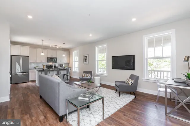 a living room with couches a coffee table a flat screen tv and kitchen view