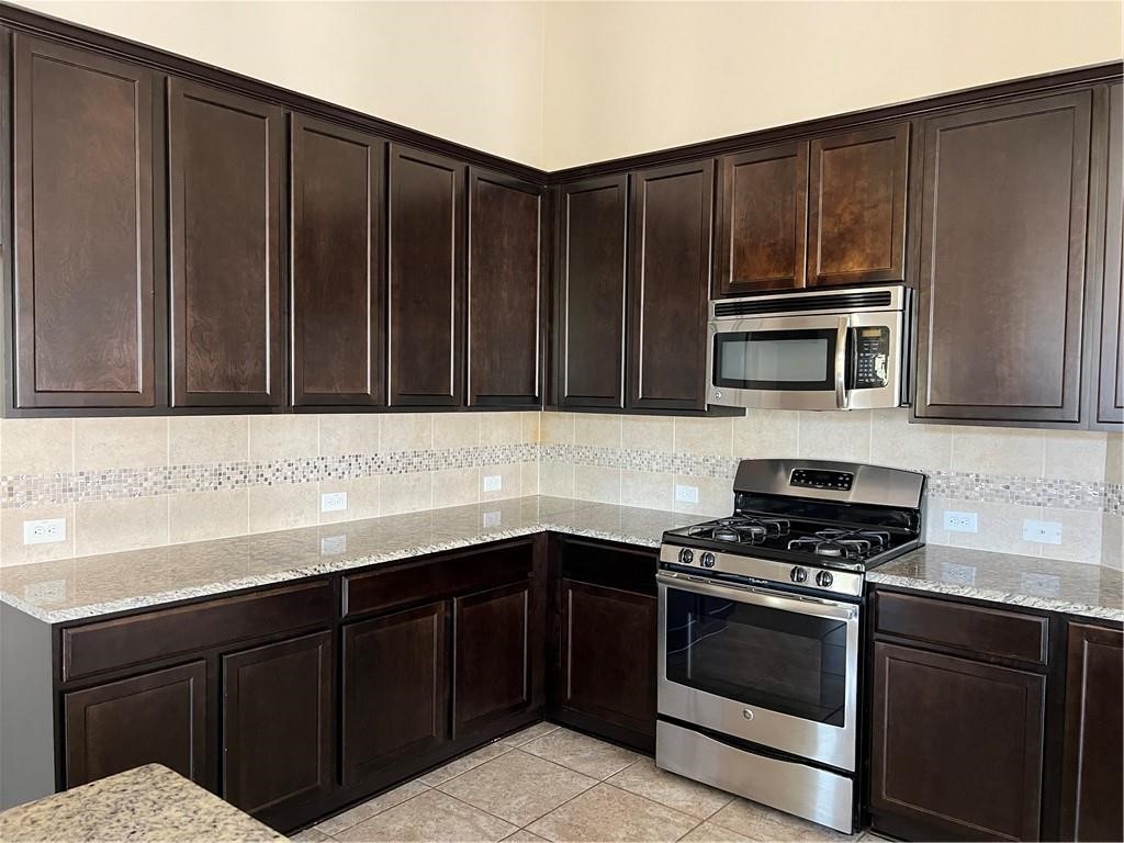 3645 Rams Horn Way Round Rock, TX 78665 - Photo 11 of 16 Kitchen featuring stainless steel appliances, dark wood finish cabinets, light stone countertops, and tasteful backsplash