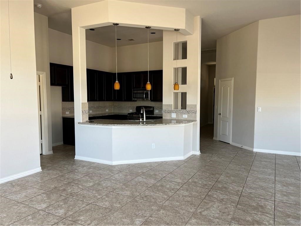 3645 Rams Horn Way Round Rock, TX 78665 - Photo 5 of 16 Kitchen featuring dark cabinetry, a high ceiling, decorative light fixtures, stainless steel microwave, and gas range oven