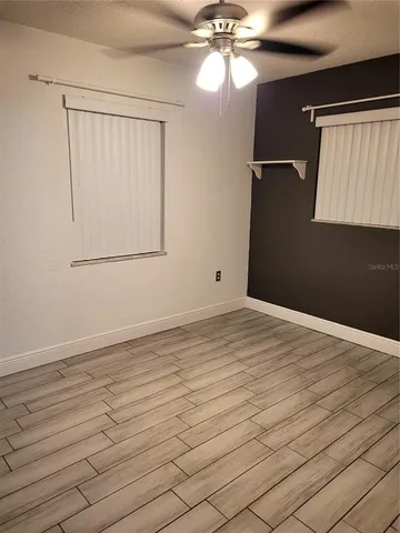 an empty room with wooden floor fan and windows