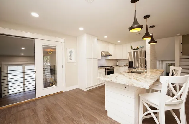 a kitchen with stainless steel appliances kitchen island granite countertop a refrigerator a stove and white cabinets with wooden floor