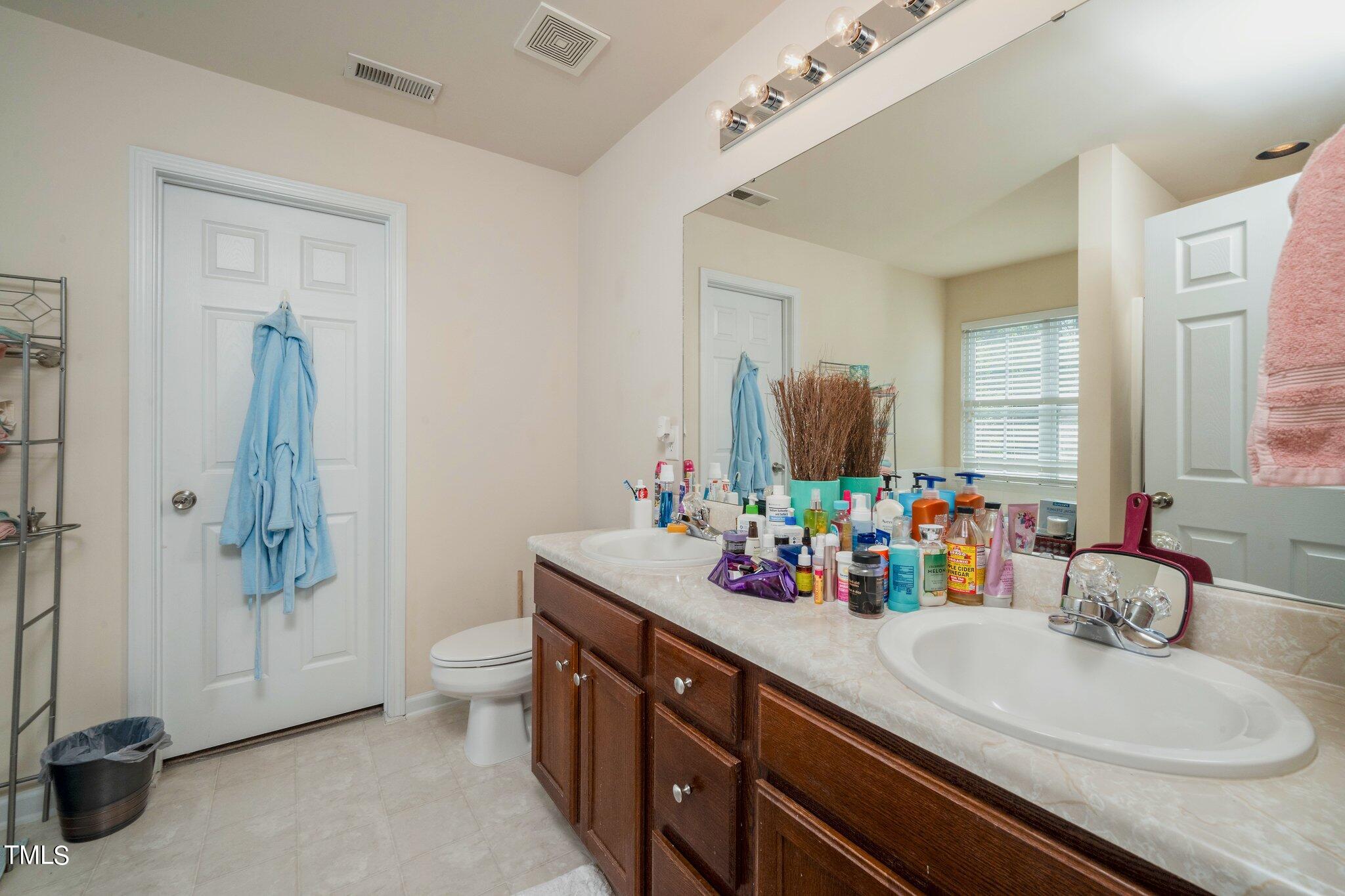 9828 Layla Avenue Raleigh, NC 27617 - Photo 13 of 21 a bathroom with double vanity sinks a toilet a mirror and shower