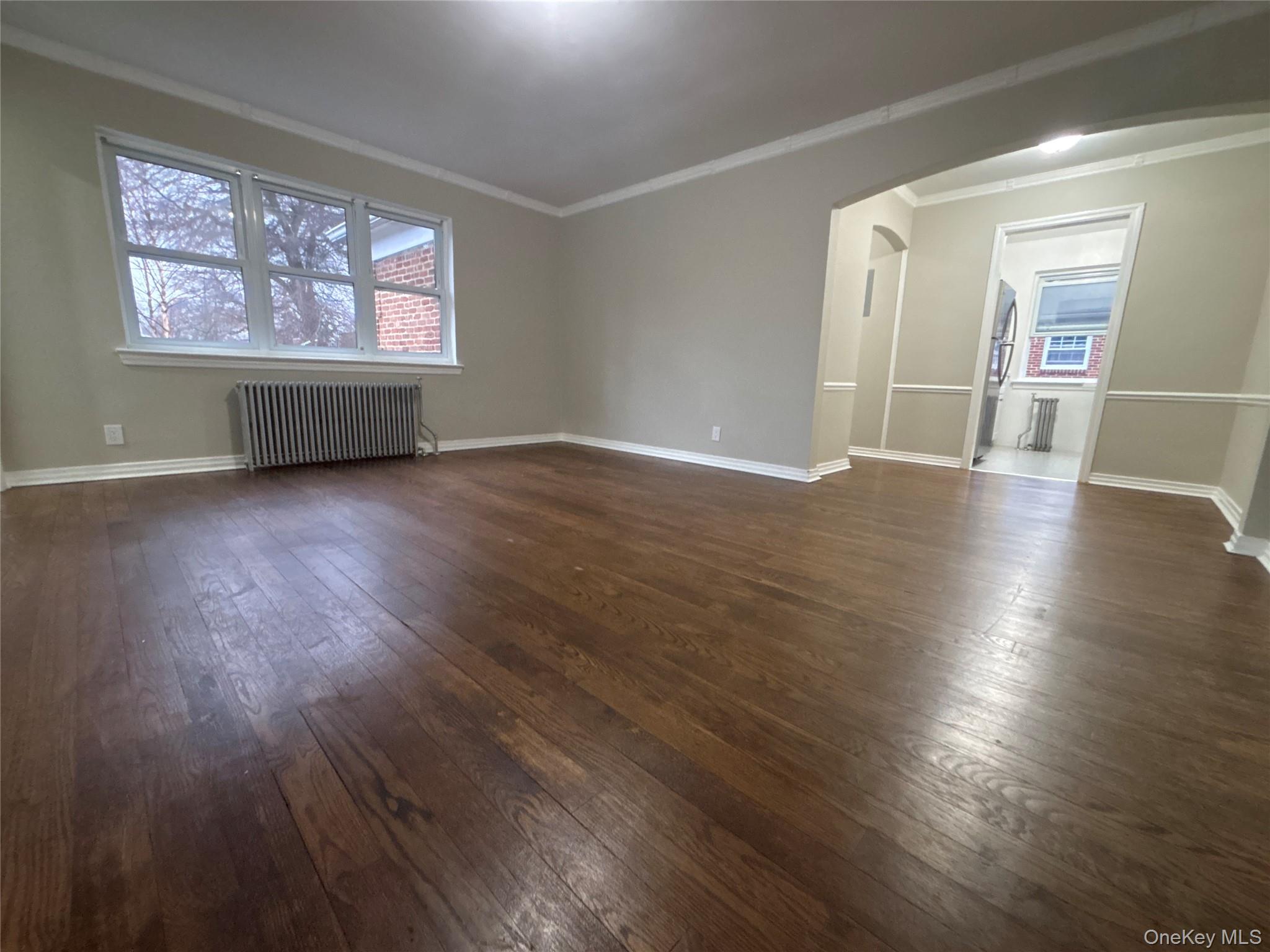 37 Spruce Street, Unit 3 Great Neck, NY 11021 - Photo 2 of 15 Empty room with arched walkways, radiator, ornamental molding, and dark wood finished floors