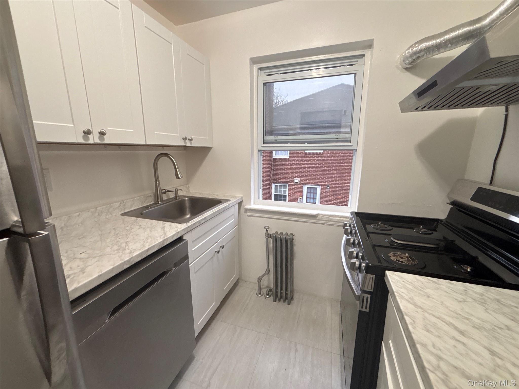 37 Spruce Street, Unit 3 Great Neck, NY 11021 - Photo 5 of 15 Kitchen featuring stainless steel appliances, range hood, white cabinets, and radiator