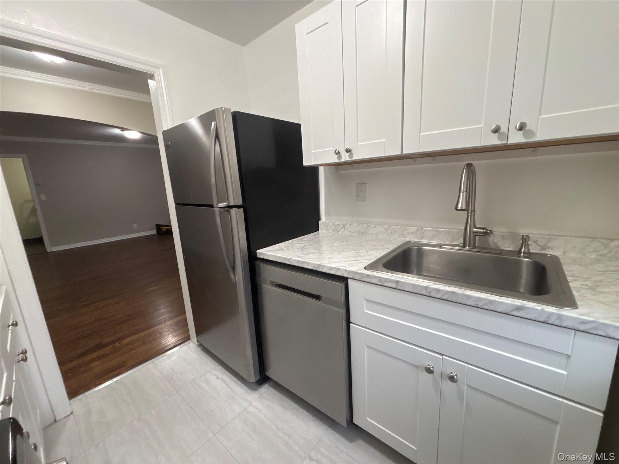 37 Spruce Street, Unit 3 Great Neck, NY 11021 - Photo 6 of 15 Kitchen featuring white cabinets, light countertops, stainless steel appliances, light tile patterned floors, and crown molding