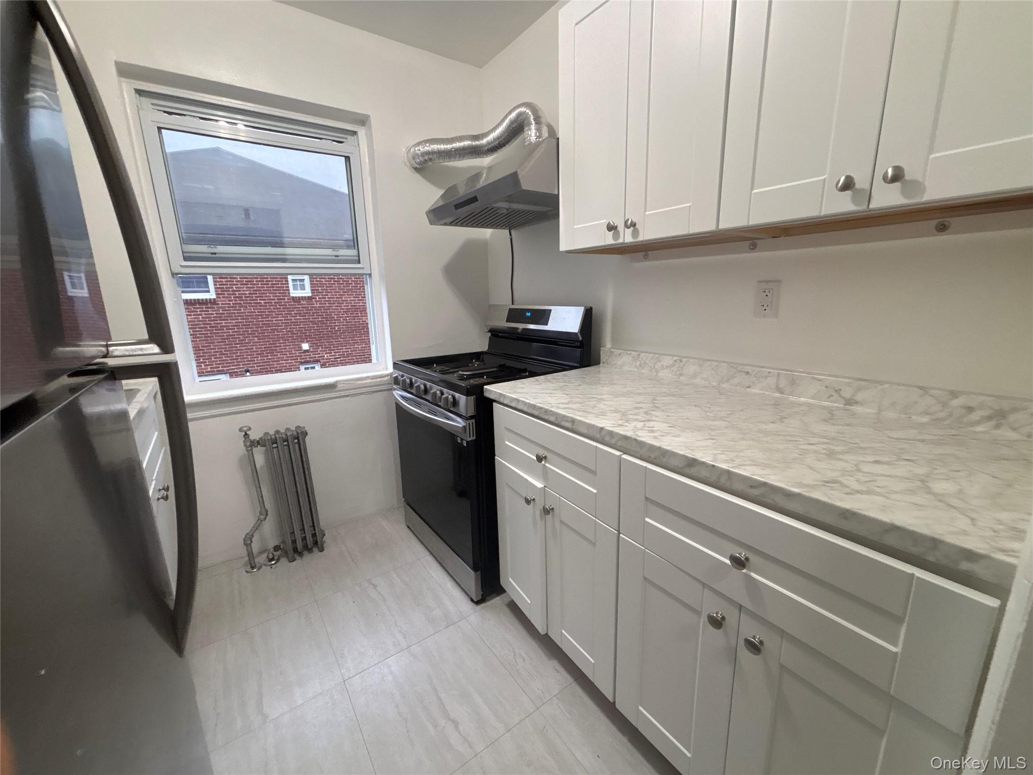 37 Spruce Street, Unit 3 Great Neck, NY 11021 - Photo 7 of 15 Kitchen with appliances with stainless steel finishes, light countertops, white cabinets, radiator, and extractor fan
