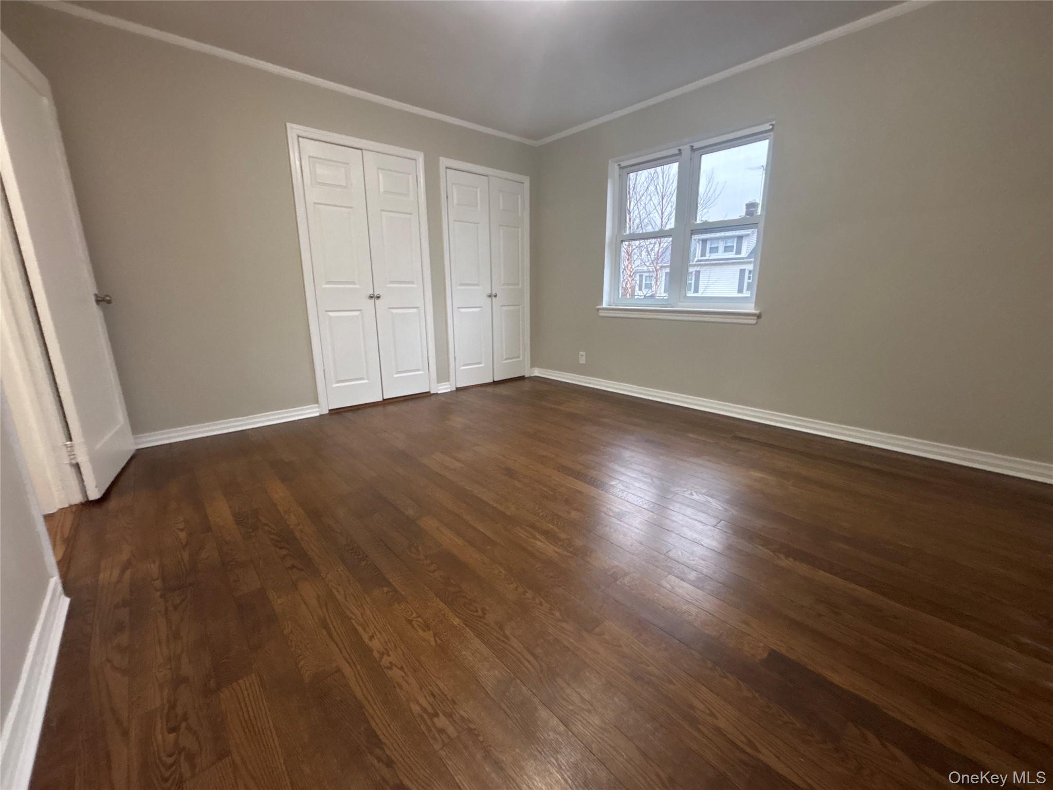 37 Spruce Street, Unit 3 Great Neck, NY 11021 - Photo 9 of 15 Unfurnished bedroom featuring multiple closets, crown molding, and dark wood-type flooring