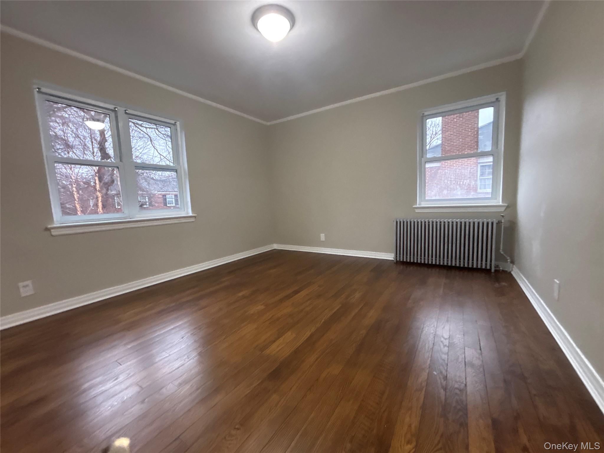 37 Spruce Street, Unit 3 Great Neck, NY 11021 - Photo 10 of 15 Unfurnished room featuring radiator, dark wood-style flooring, and crown molding