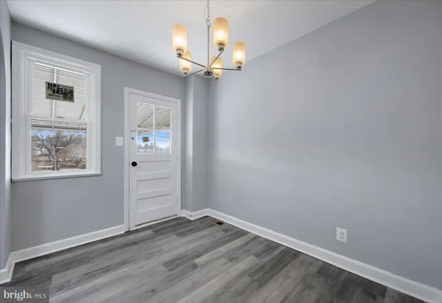 an empty room with wooden floor chandelier and windows