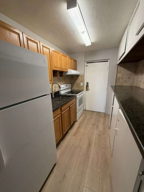 27 Gordon Street, Unit 105 Framingham, MA 01702 - Photo 2 of 7 a kitchen with granite countertop a refrigerator a sink and wooden cabinets