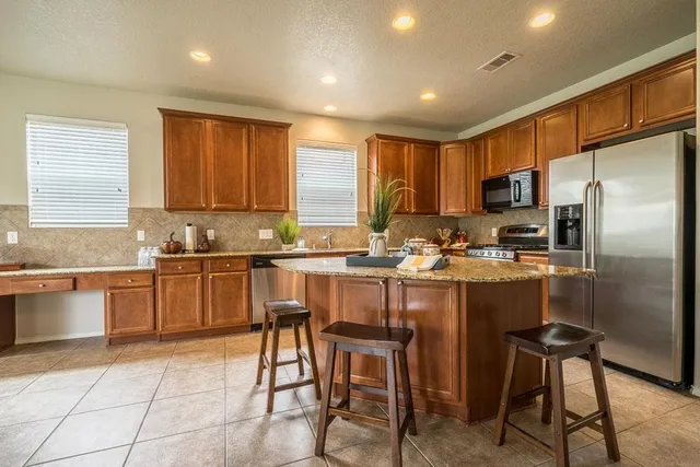 a kitchen with stainless steel appliances granite countertop a stove a sink a refrigerator and chairs