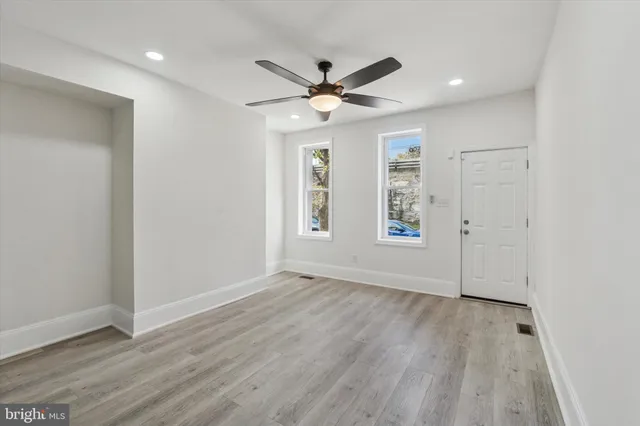 an empty room with wooden floor ceiling fan and windows