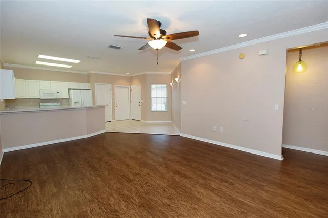 a view of an empty room with wooden floor and a ceiling fan