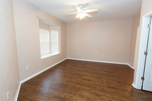 an empty room with wooden floor fan and windows
