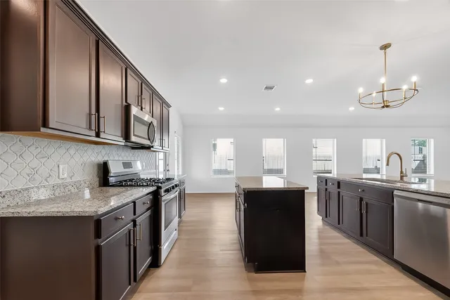 a large kitchen with stainless steel appliances granite countertop a sink dishwasher stove and wooden cabinets