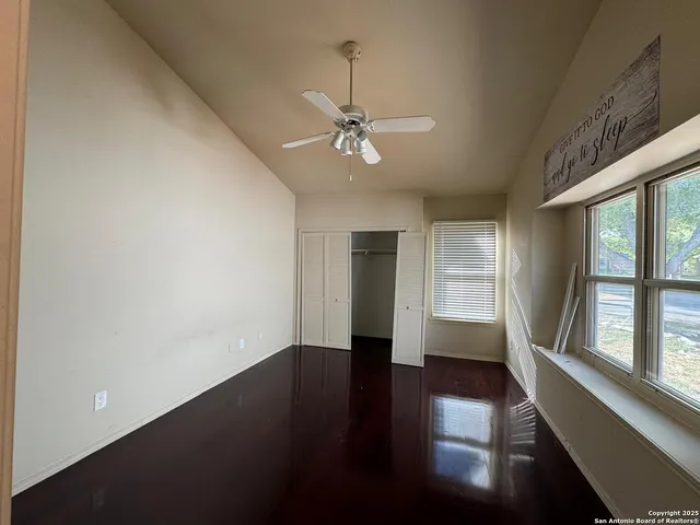 an empty room with wooden floor fan and windows