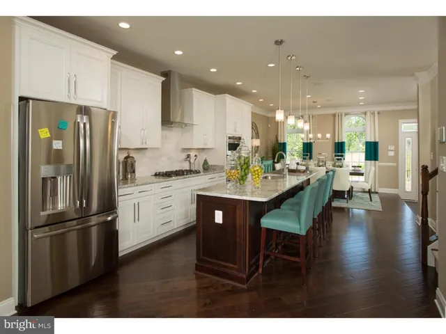 a kitchen with stainless steel appliances kitchen island granite countertop a refrigerator a sink dishwasher a stove and white cabinets with wooden floor