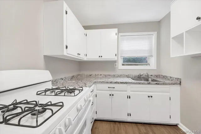 a kitchen with stainless steel appliances granite countertop a sink stove oven and white cabinets with wooden floor