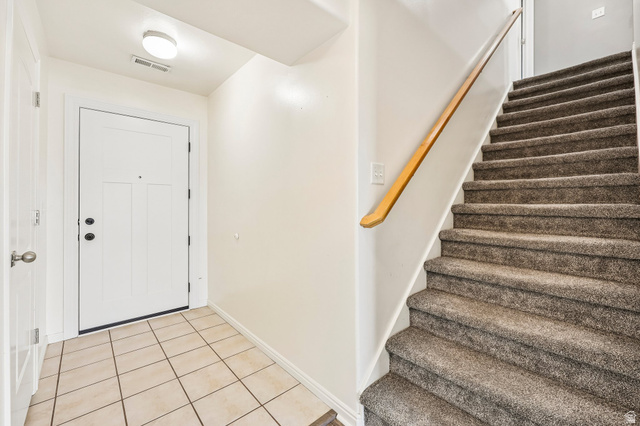3215 West 450 North West Point, UT 84015 - Photo 3 of 40 Entryway featuring a white paneled door with dark hardware, square tile flooring, and a carpeted staircase with a wood handrail