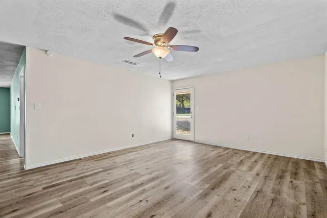 an empty room with wooden floor fan and windows