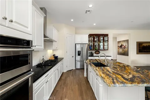 a kitchen with stainless steel appliances granite countertop a stove top oven a sink a refrigerator white cabinets and wooden floor